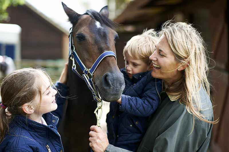 Mature woman with son and daughter petting horse 
