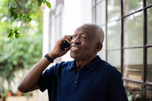 Older black man smiling talking on the phone outside